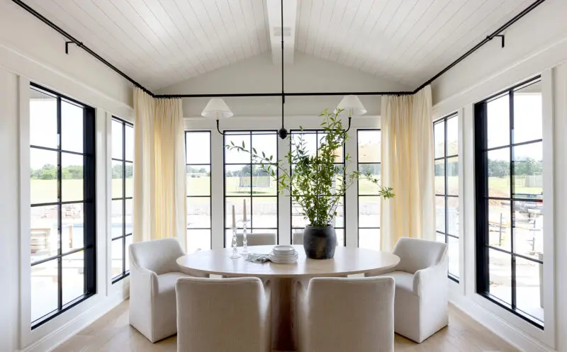 A round table with six fabric chairs tucked into a room full of windows.