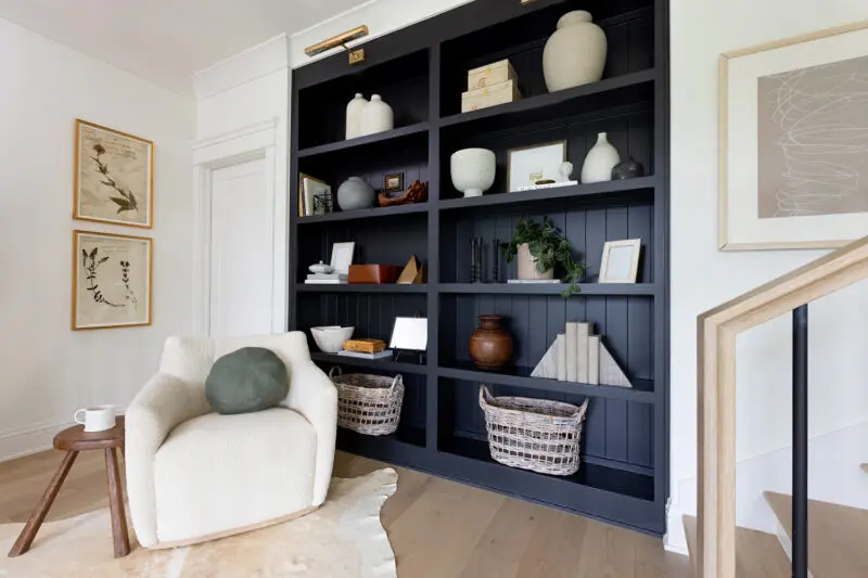 A reading nook at the top of a staircase with a chair and decorrative black bookshelf.