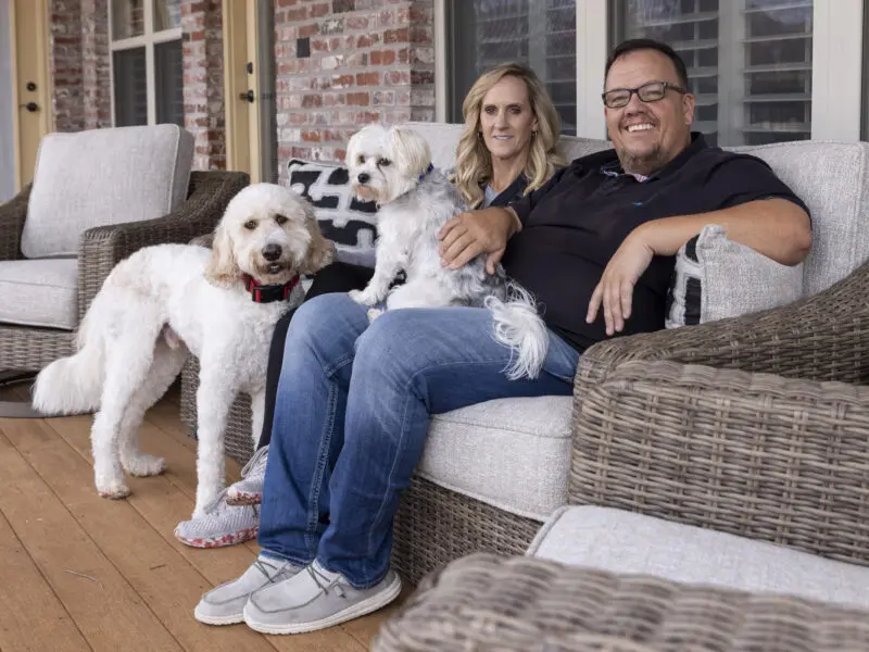 Portrait of a man and woman with two white dogs on their back porch in Rogers.