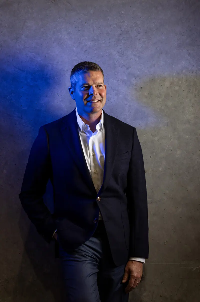 An executive stands near a concrete wall and has a blue light on his face.
