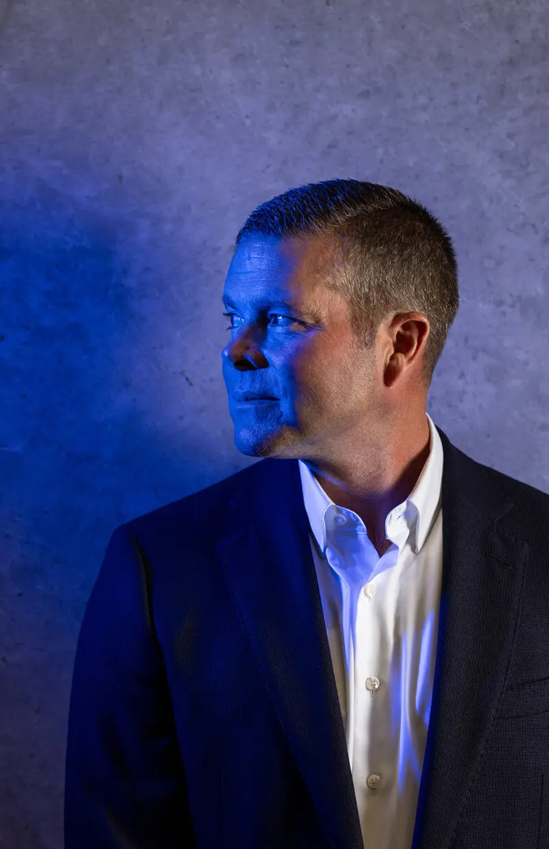 An executive stands near a concrete wall and has a blue light on his face.