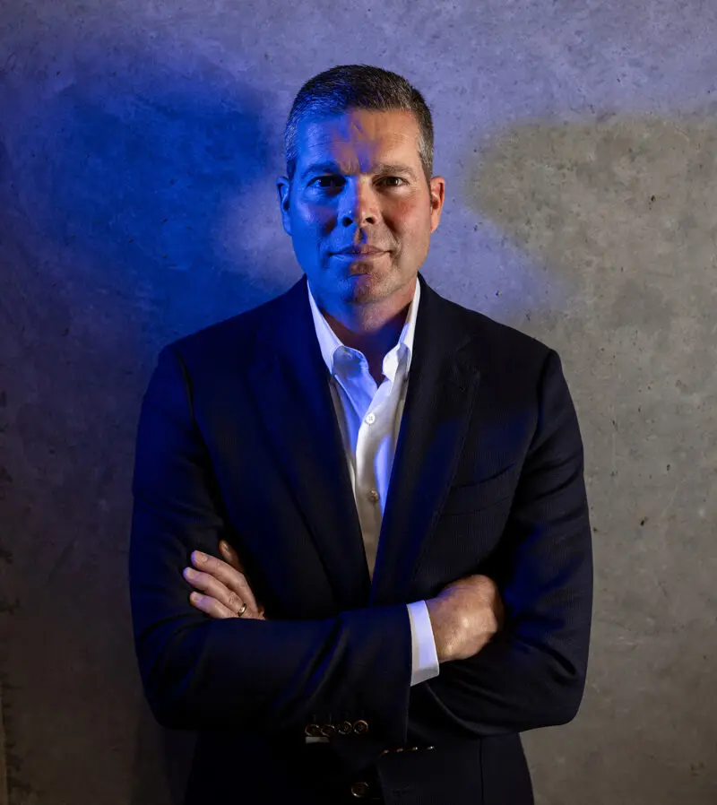 An executive stands near a concrete wall and has a blue light on his face.
