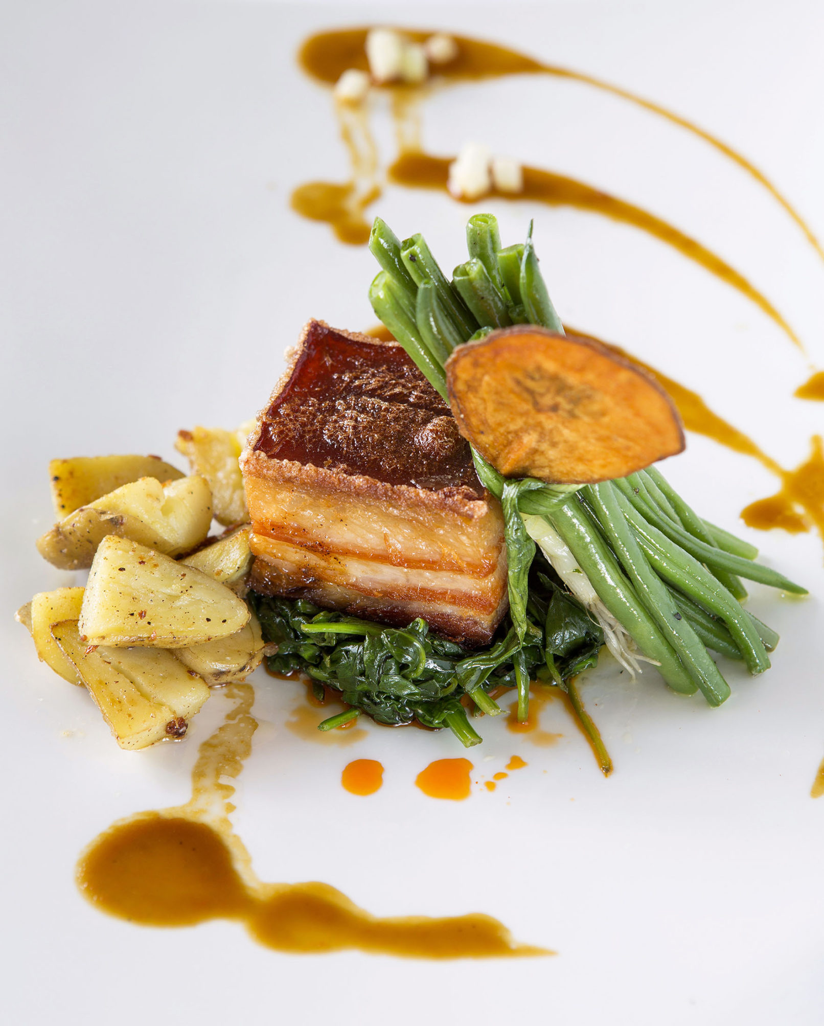 Food photography of pork belly served over greens on a white plate.