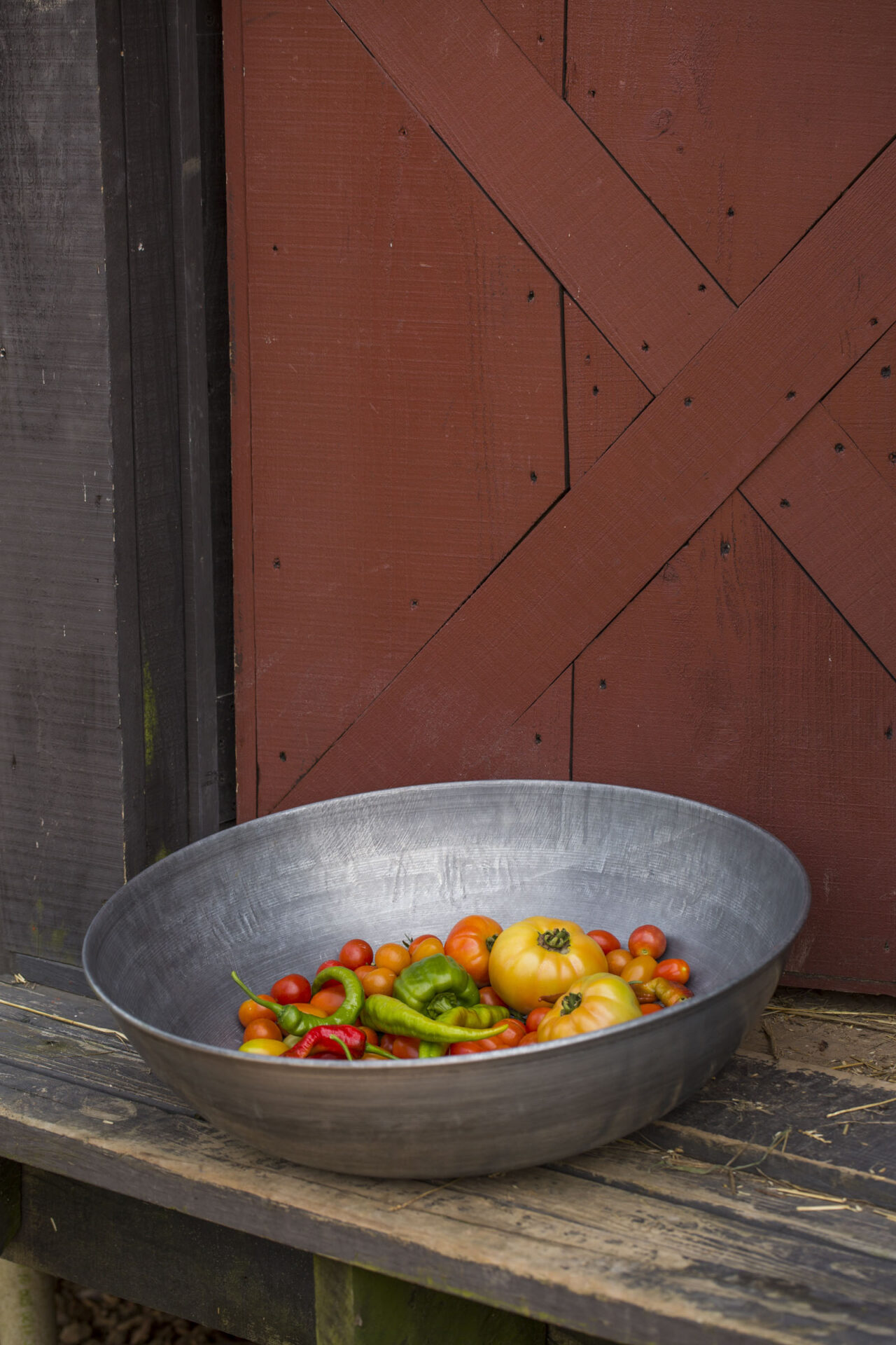 Product photography of a bowl of freshly picked garden vegetables near a barn.