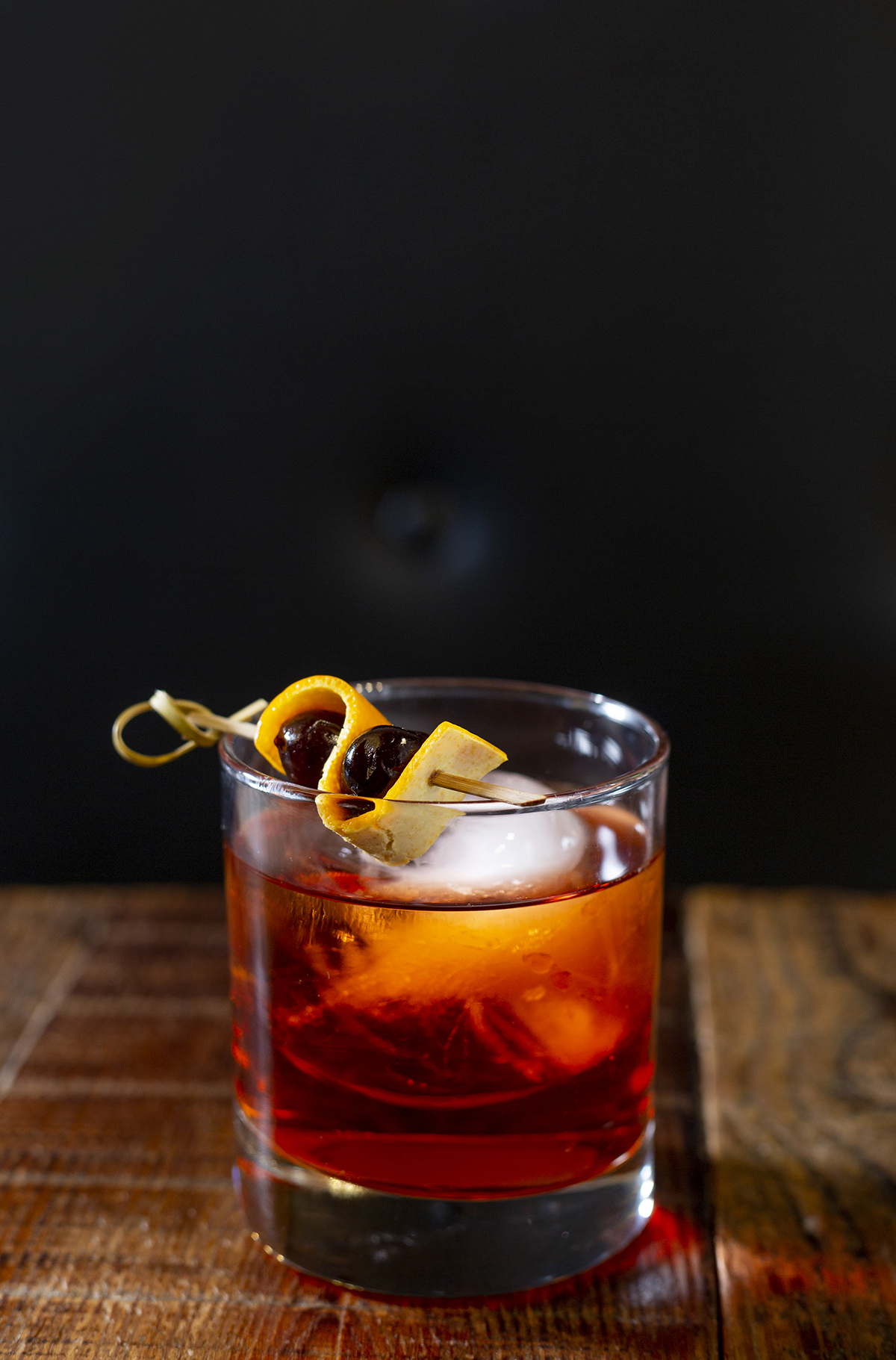 A whiskey drink on a wooden table with a dark background and smokey light