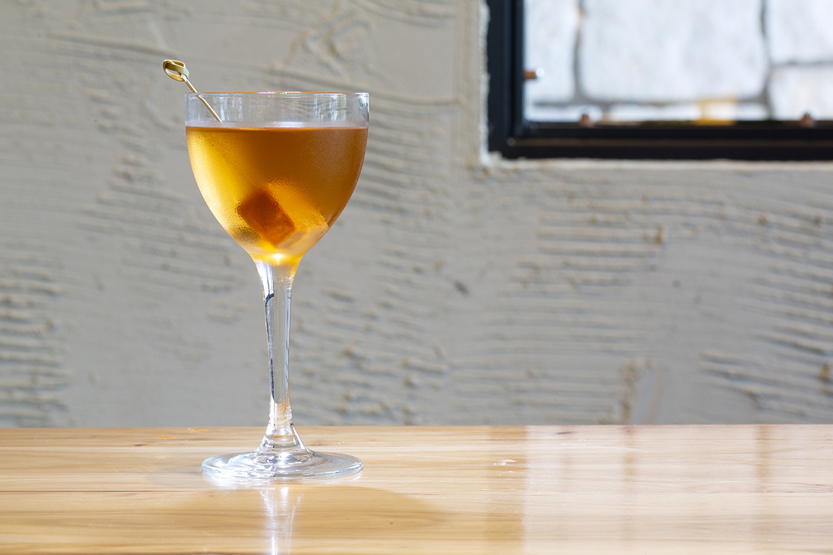 Photography of a single glass with a caramel as garnish, photographed against a white wall near a window.