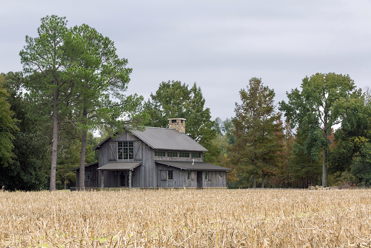 Exterior photography of a lodge with rustic wooden siding near a corn field, and surrounded by pine trees.