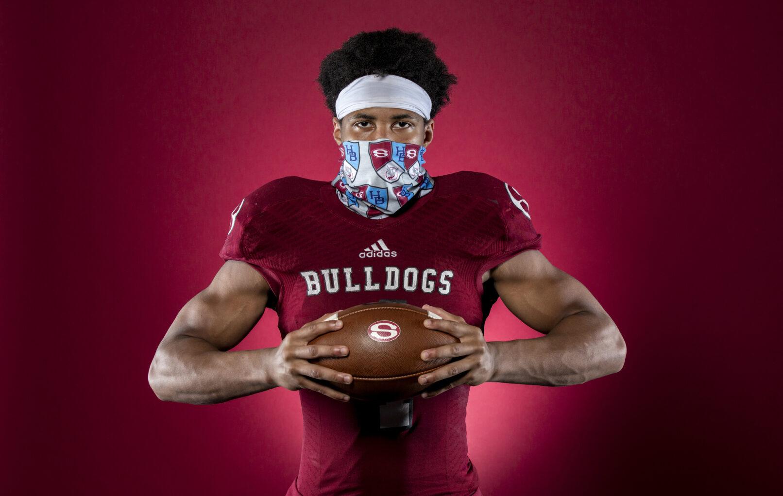 Portrait of a football player wearing a mask standing in front of red background.