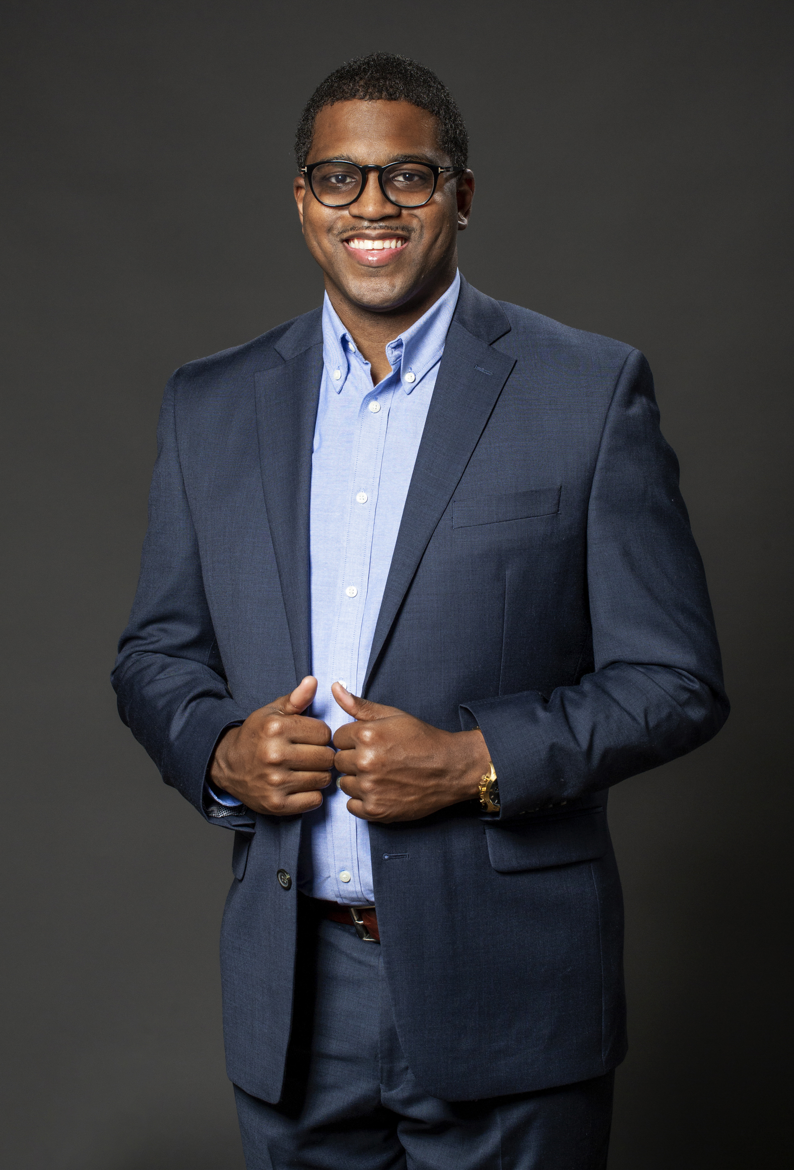 Headshot of a Black man wearing glasses on a gray background