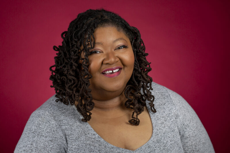 portrait of a Black woman taken in a photography studio on a red background.