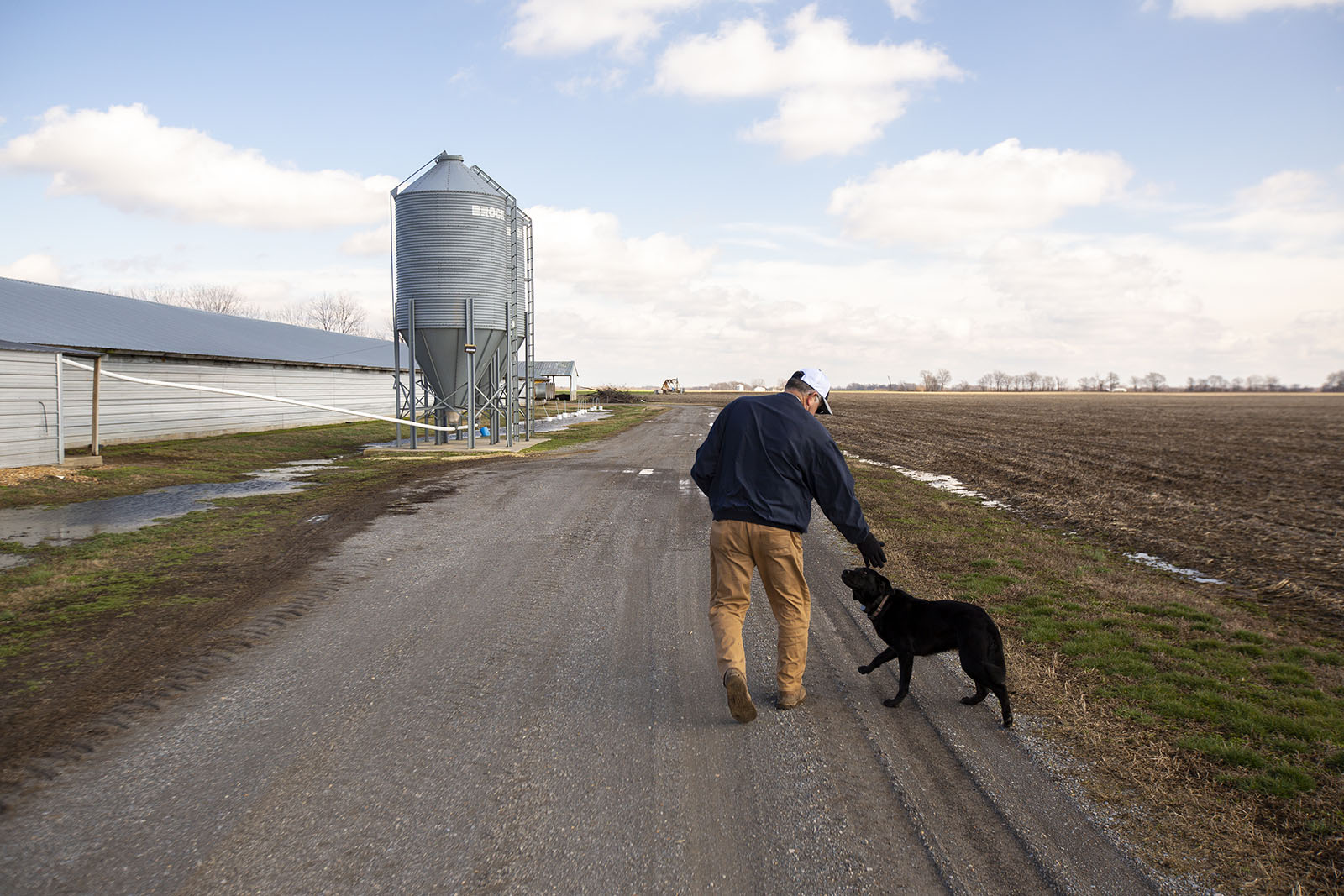 A farmer walks around his chicken farm with his black lab.