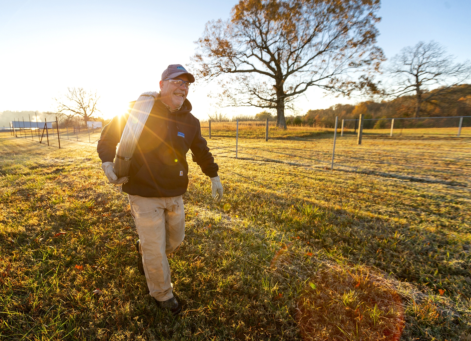 Portrait of a man carrying a coil of metal through a field in the early morning.