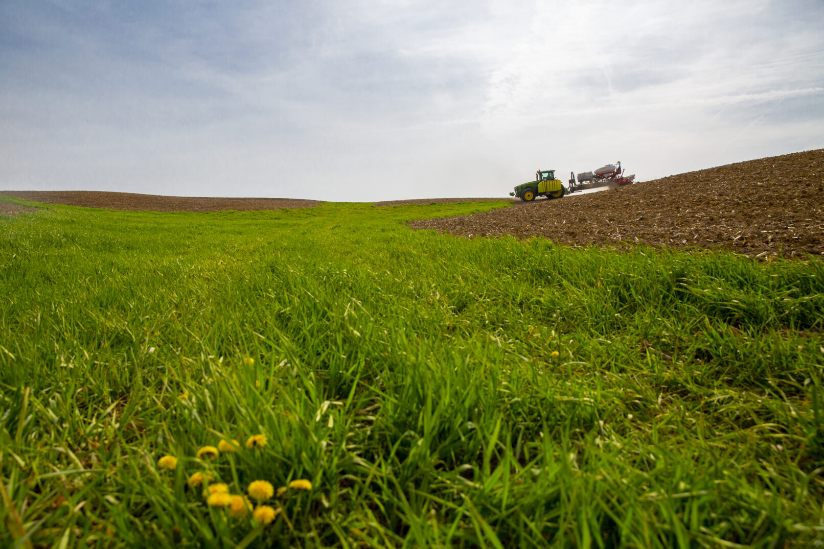 A farmer plows dirt while driving a tractor next to a green field of grass.