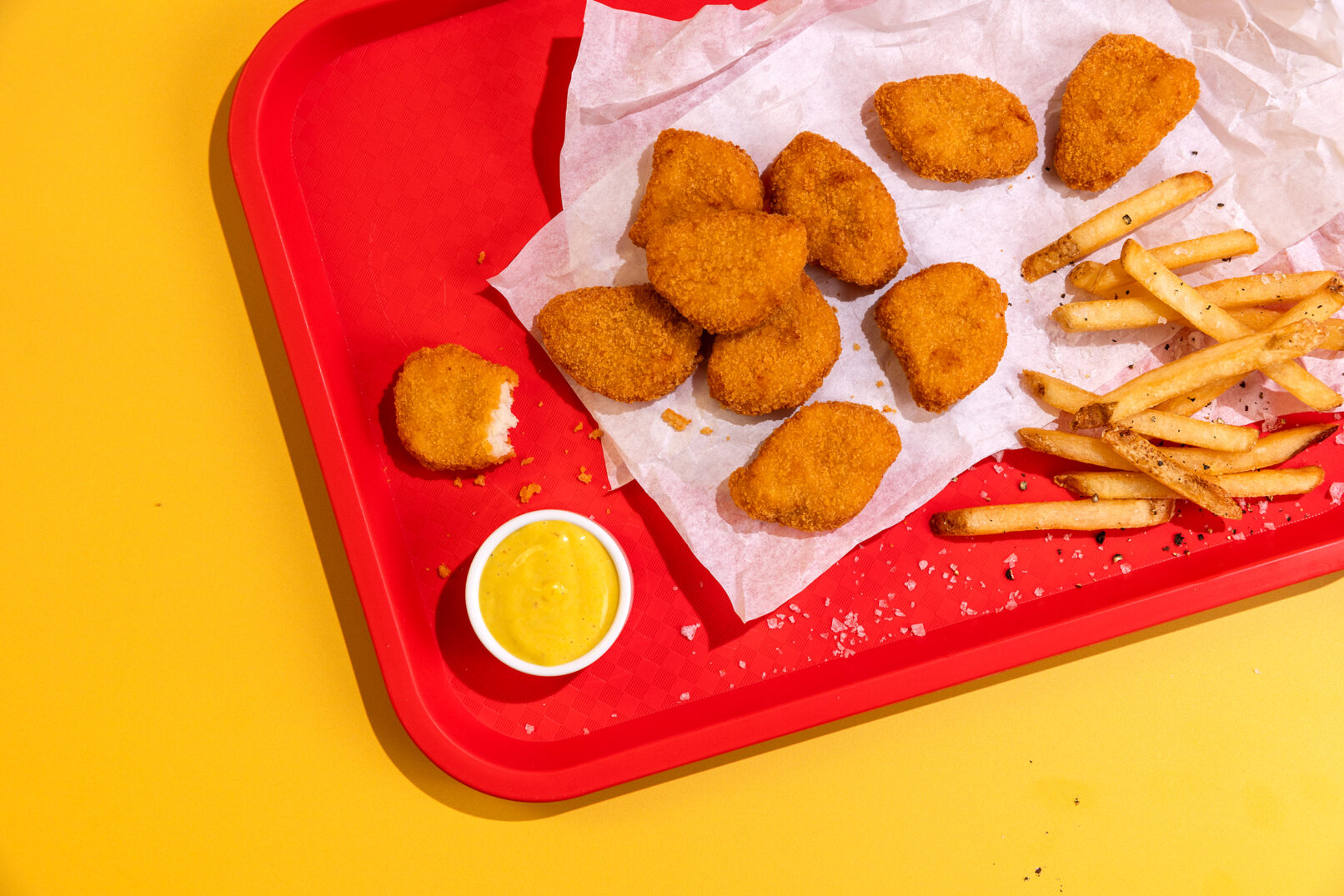 Photography of chicken nuggets on a red tray and a yellow background with french fries.