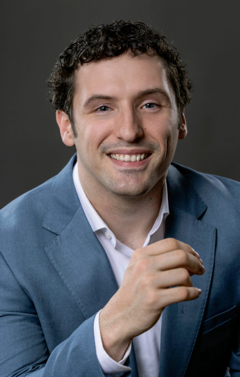 Studio headshot of a white man on a gray background using professional lighting.