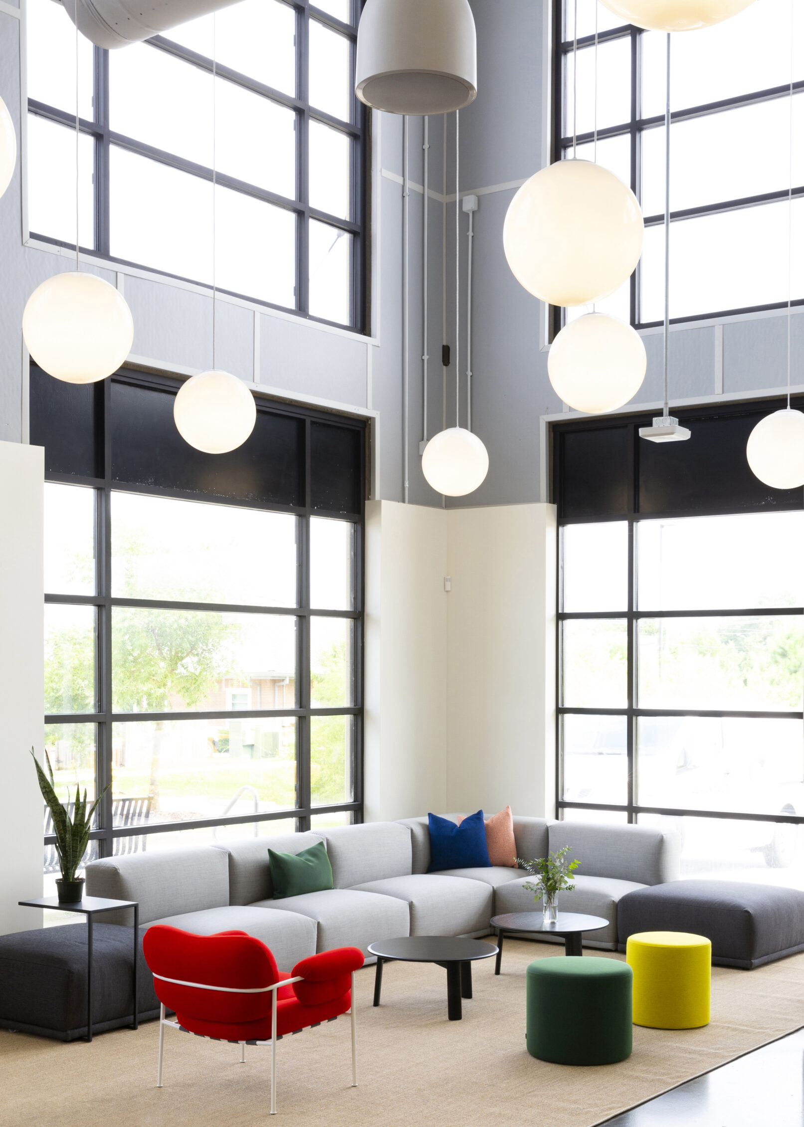 Interior of a commercial building with large windows, large round lighting and colorful furniture.