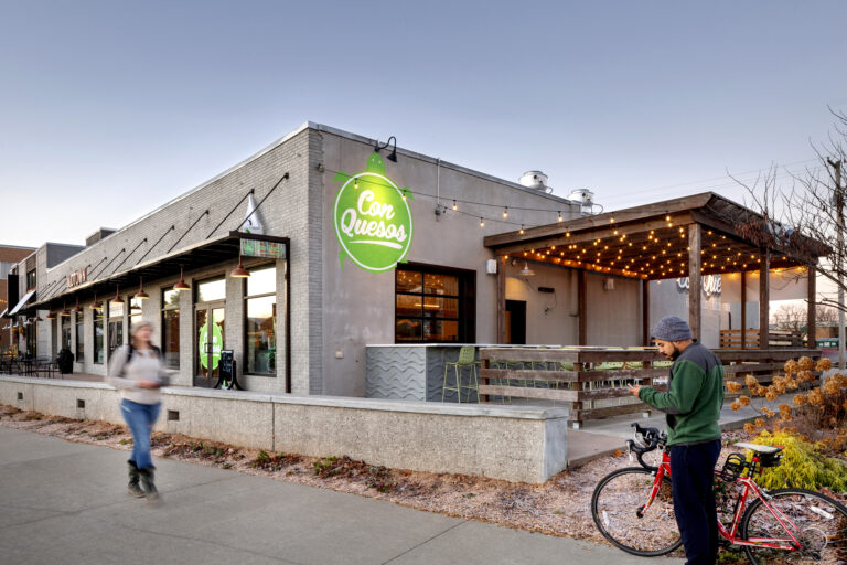 Photography of the exterior of a building as people walk and bike past.