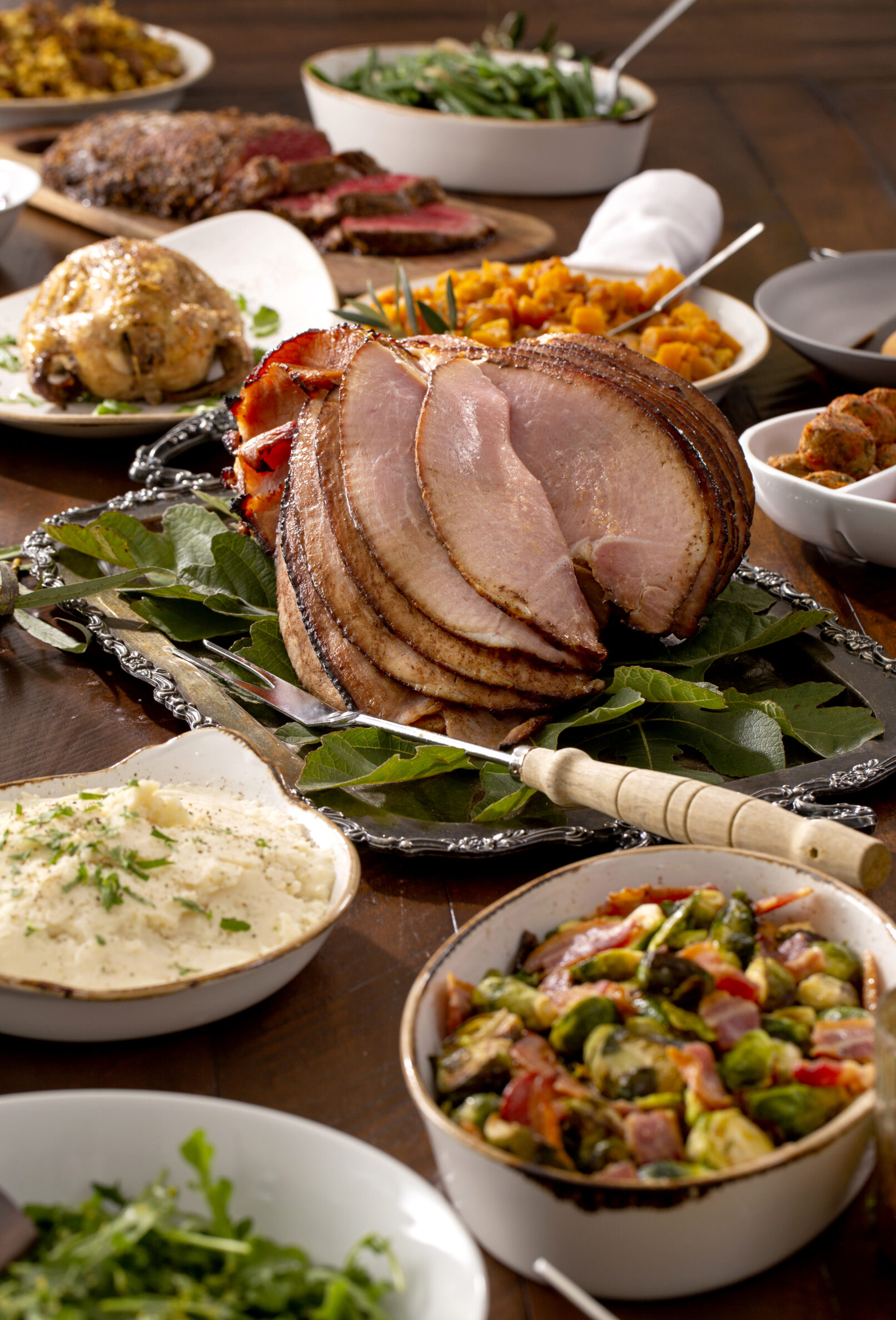 Photo of a Thanksgiving tablescape with ham, salad, green beans, mashed potatoes and other traditional foods.