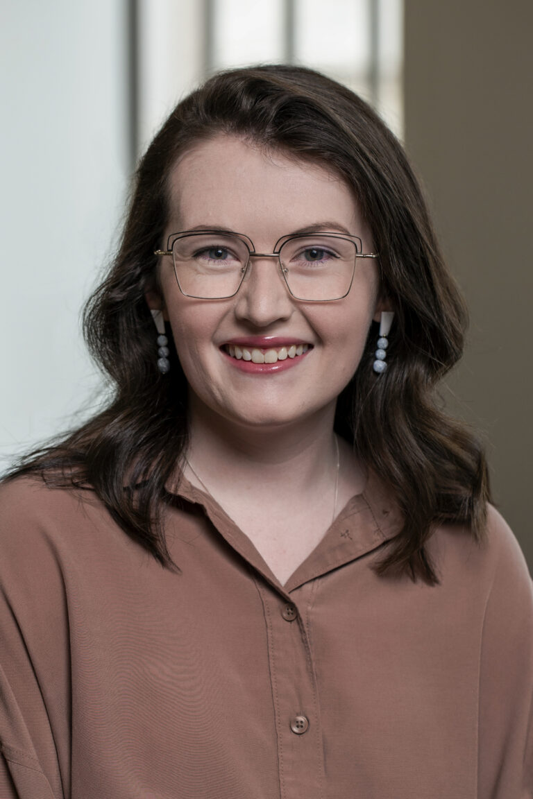 Head Shot of a woman in a beige shirt taken in front of a window.