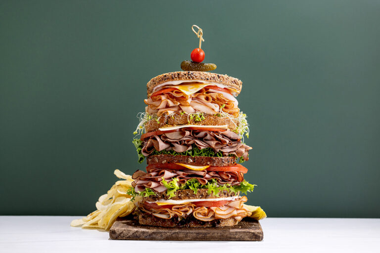 Four section tall dagwood sandwich on a white table with a green background.