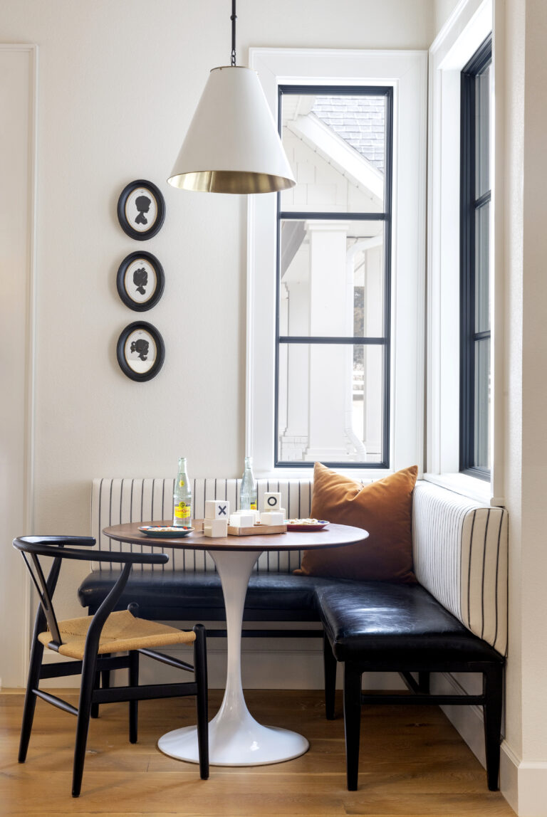 A breakfast nook with ba black bench and white table.