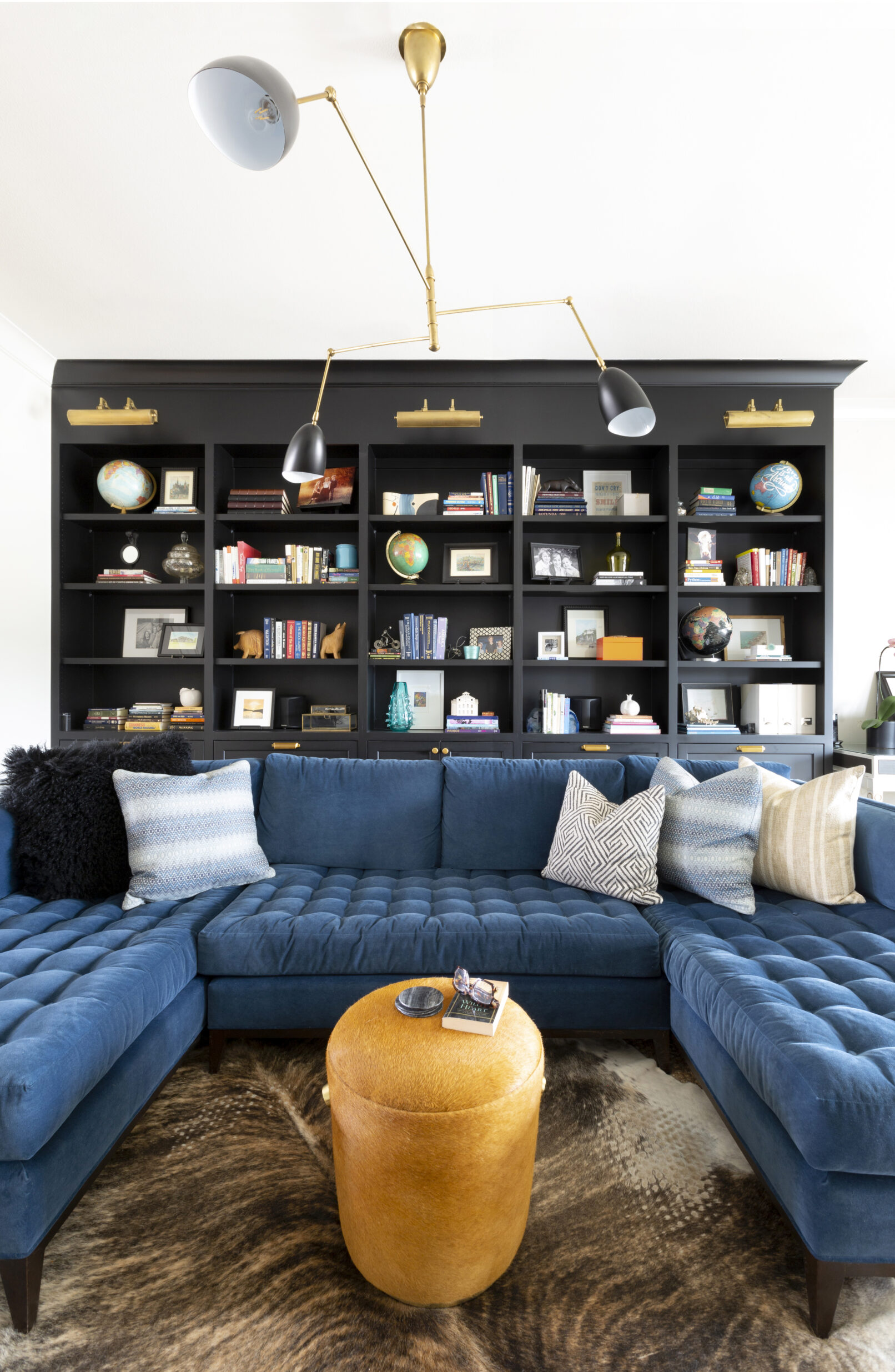 Interior of a living room with a blue couch, black bookshelves and a large funky light fixture.