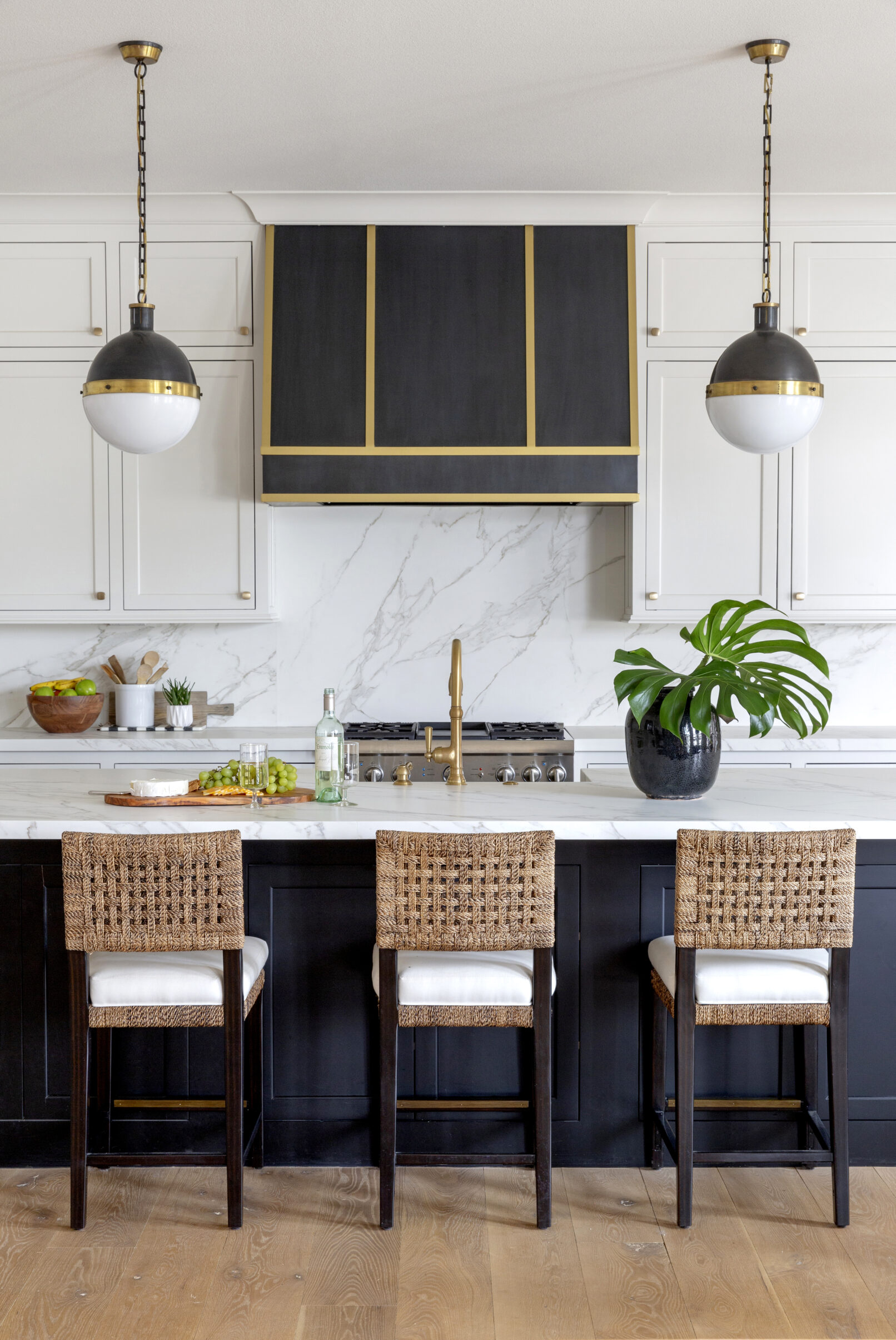 Interior photography of a white kitchen with black cabinets, three rattan chairs and gold accent details.