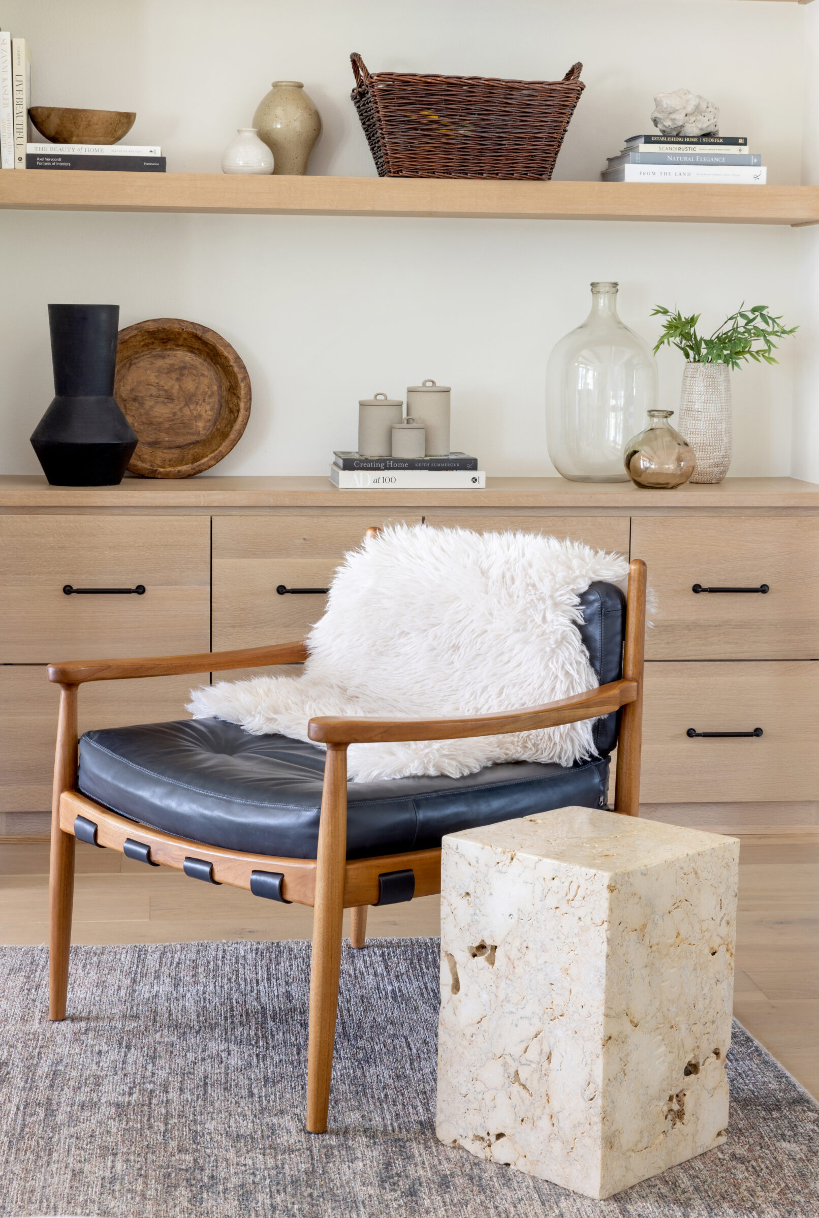 A mid century chair with black leather sits in front of a bookcase in this interior photo.