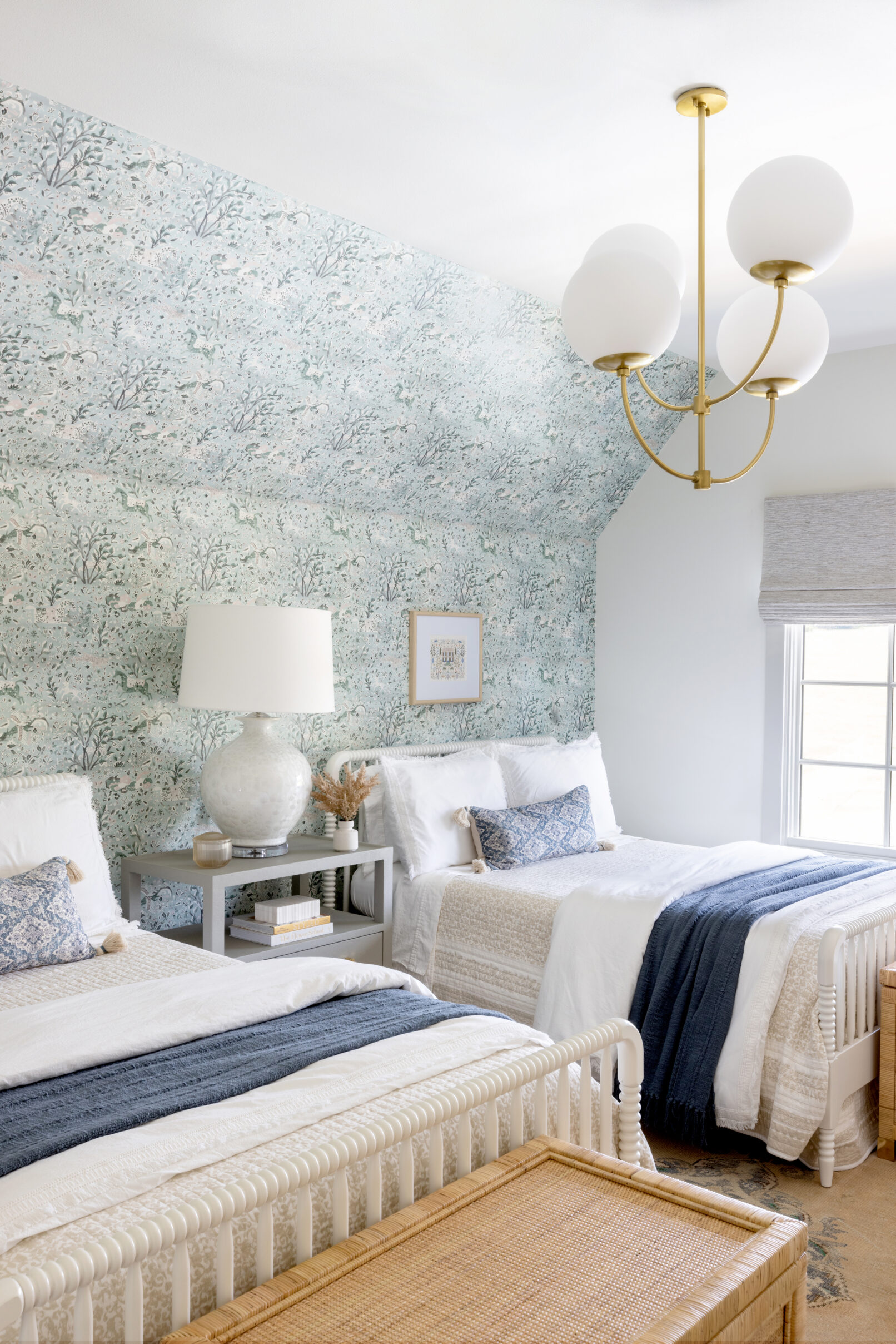 Interior photography of A child’s bedroom with blue floral wall paper, white bedding and a gold light fixture.