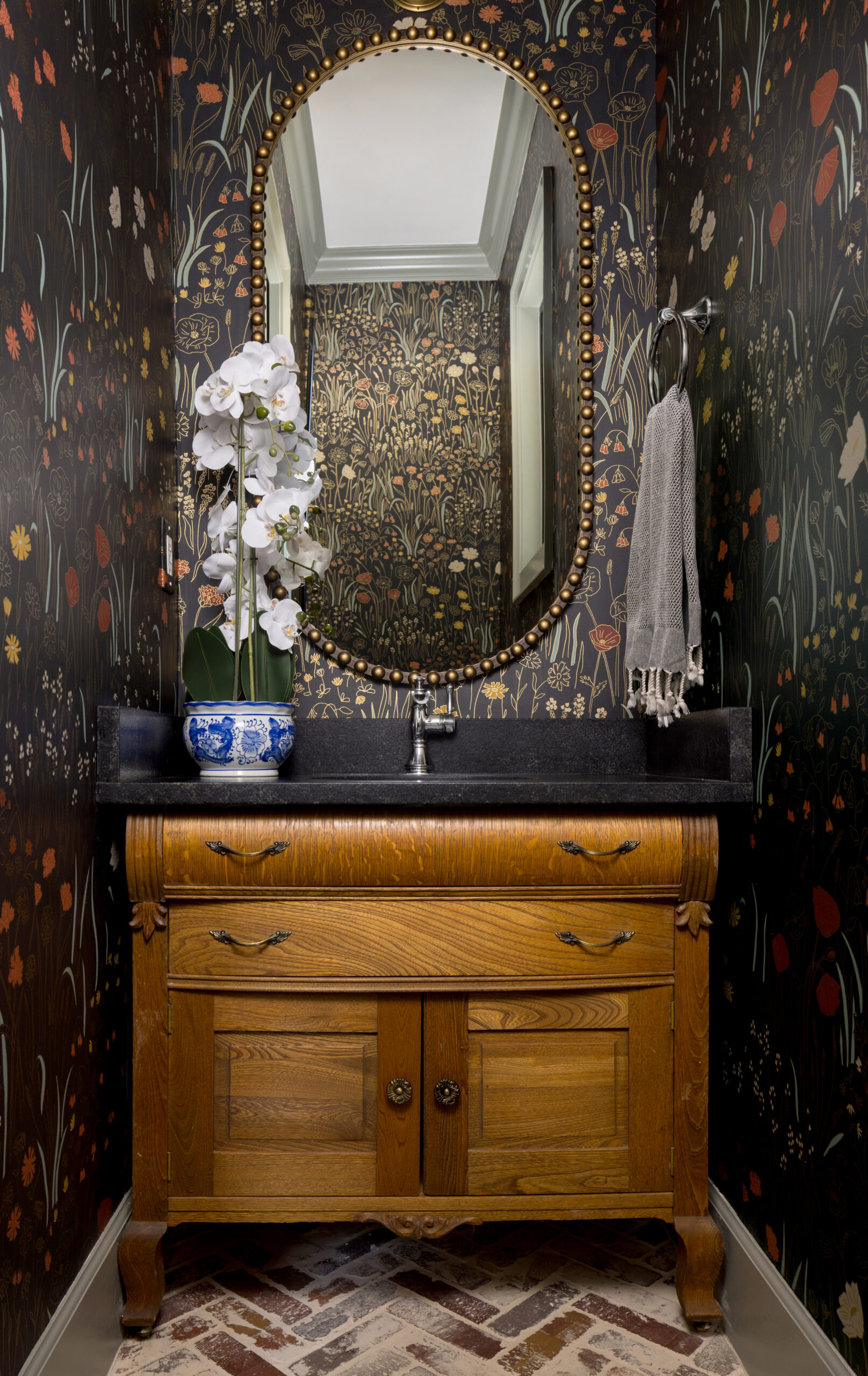 Interior photo of a bathroom with black decorative wallpaper, a gold mirror and wood chest for a cabinet.