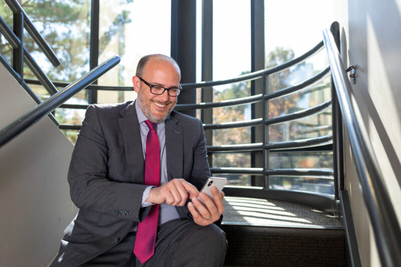 Portrait of an attorney typing on a phone while sitting in a stairwell.