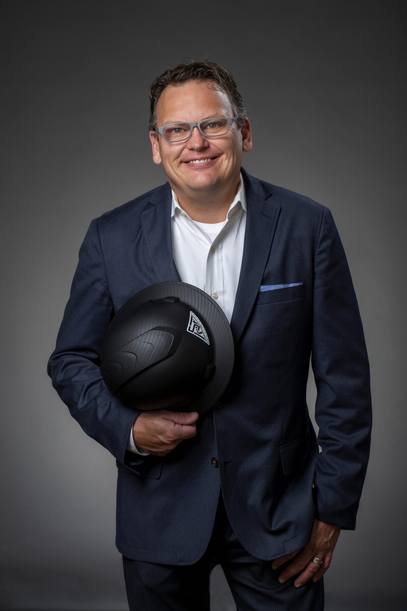 Studio portrait of a man in a suit holding a hardhat on a gray backgound.