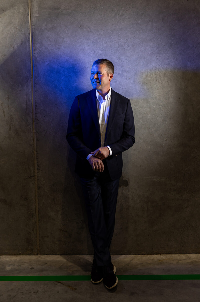 An executive stands near a concrete wall and has a blue light on his face.